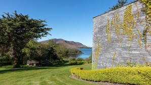 Un bâtiment à la façade en pierre et orné de lierre jaune, entouré de pelouse bien entretenue et d’un petit étang.