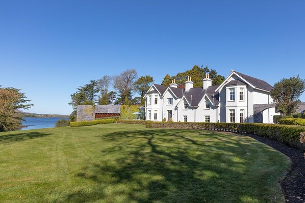 A large, white, two-story house with a well-maintained lawn and a view of a lake.