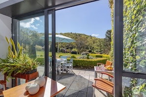 Une terrasse extérieure avec une table et des chaises, un pot de fleurs et une vue sur un jardin aménagé et des collines.