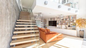 Un salon moderne avec un escalier, un canapé, une bibliothèque et un téléviseur.