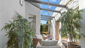 Un espace extérieur moderne, aménagé avec des meubles en osier, des plantes en pot et une structure de plafond en verre.