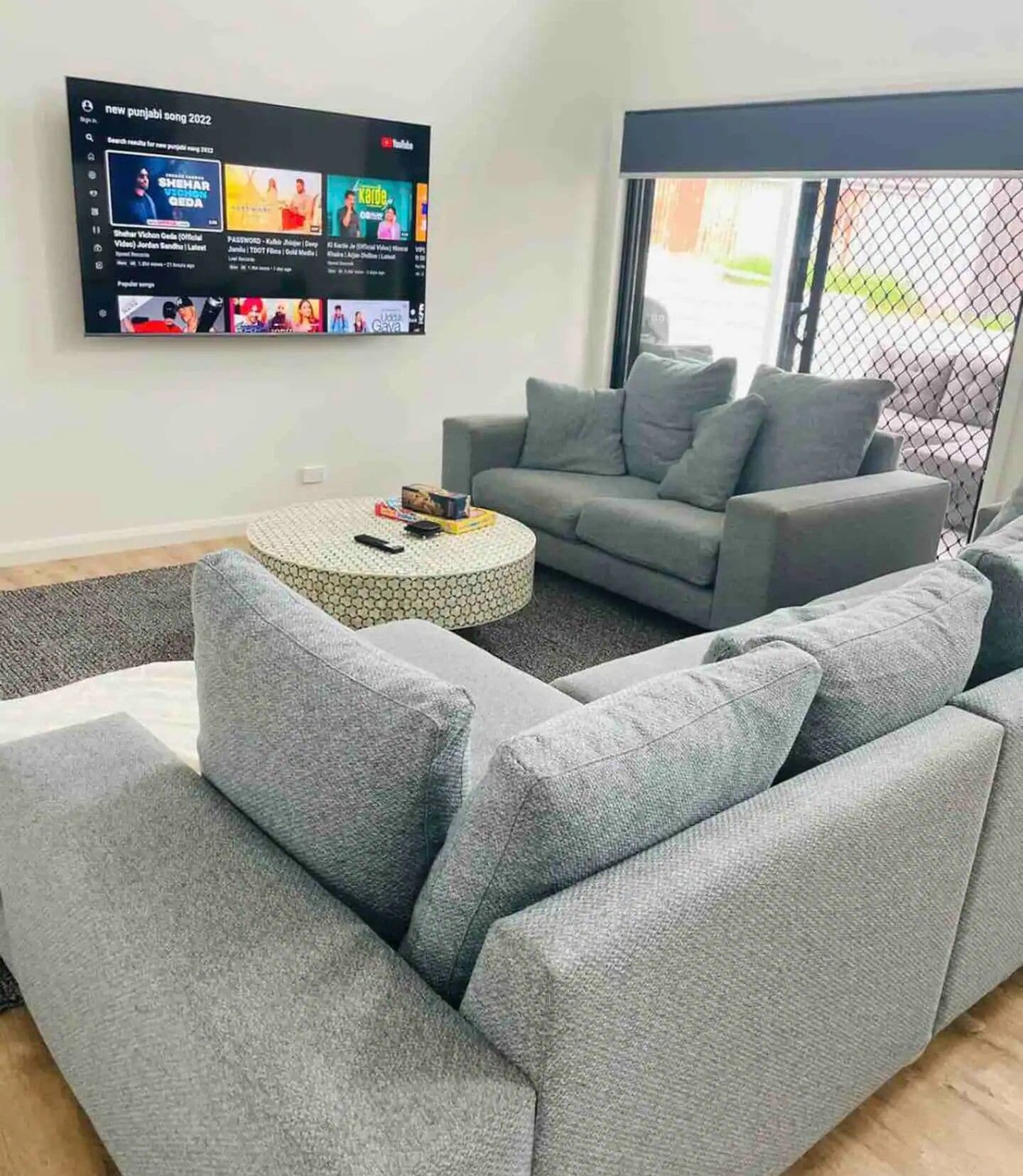 En moderne stue med en grå modulsofa, et rundt sofabord og et fladskærms-tv på væggen, der viser en musikvideo.