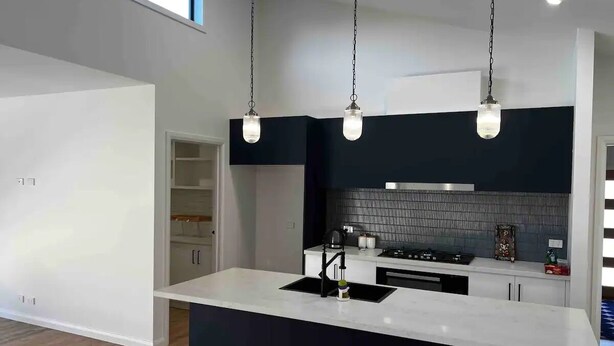 Een moderne keuken met een centraal kookeiland, een zwarte spatwand en hanglampen.