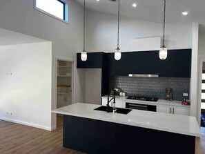 Cocina moderna con isla central, salpicadero negro e iluminación colgante.