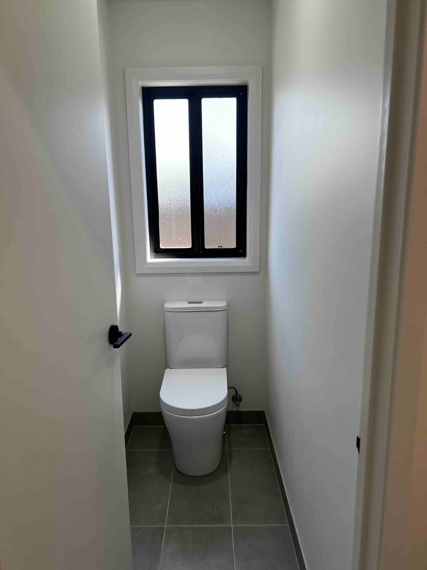 A small, clean bathroom with a toilet, a window, and a door.