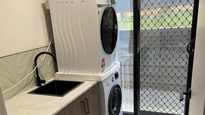 Een wasserette met een wasmachine, een wastafel en een deur naar een buitenruimte.