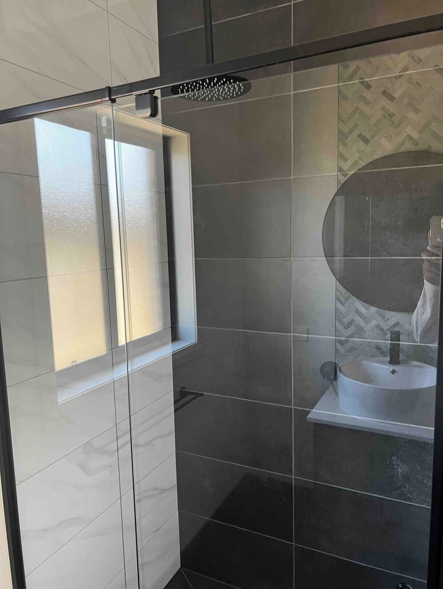 A modern bathroom with a glass shower enclosure, a large mirror, and a white sink.