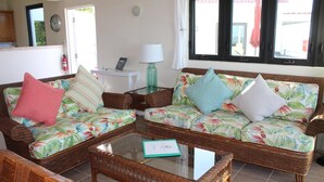 Ein Wohnzimmer mit zwei Korbschaukelsofas, einem Glastisch und einem kleinen weißen Beistelltisch mit einer Lampe.