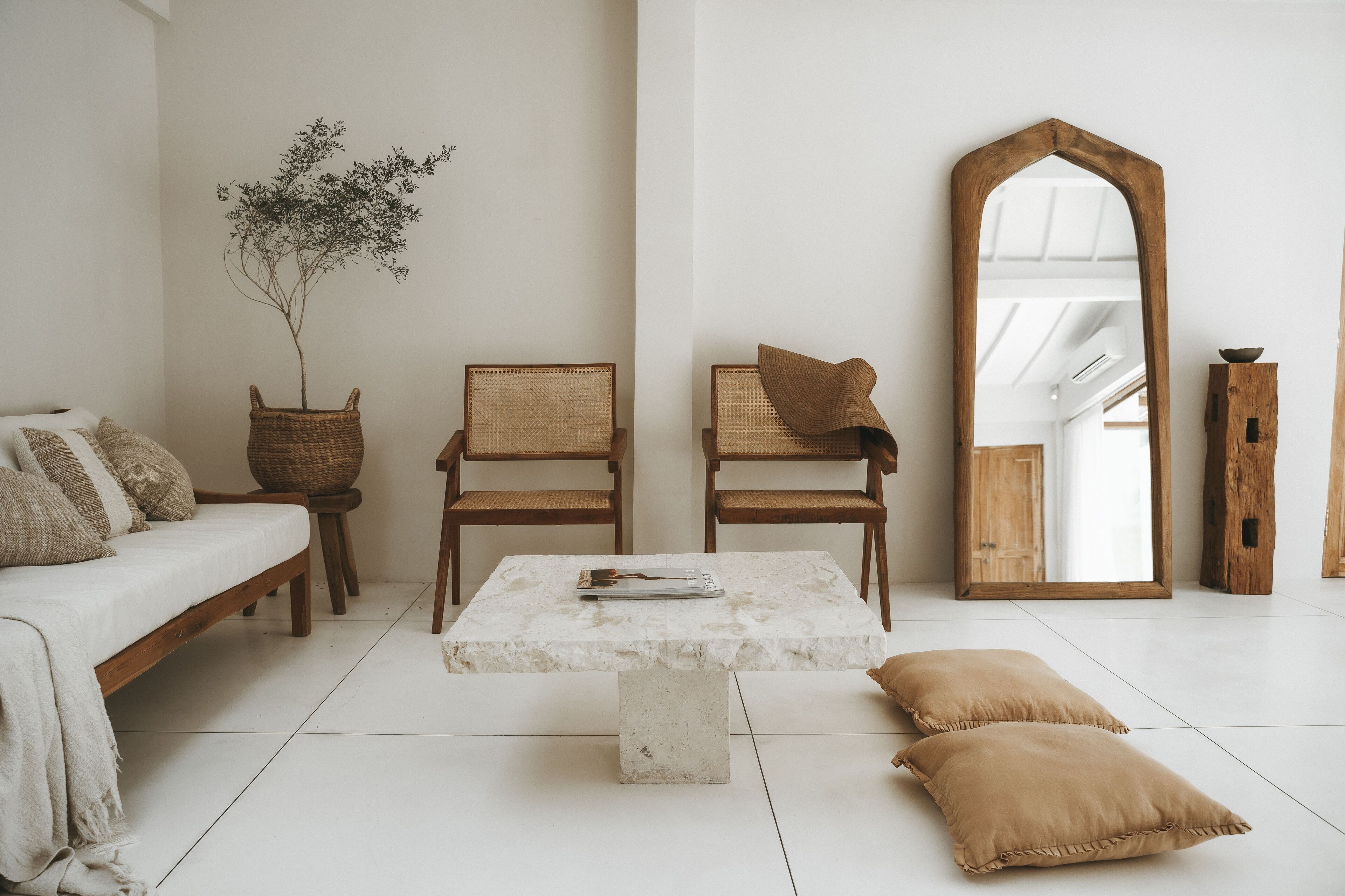 A minimalist living room with a sofa, two chairs, a coffee table, a mirror, and a plant.