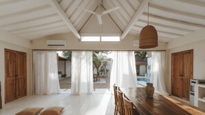 Un comedor amplio con una mesa y sillas de madera, cortinas blancas y vistas al patio exterior.