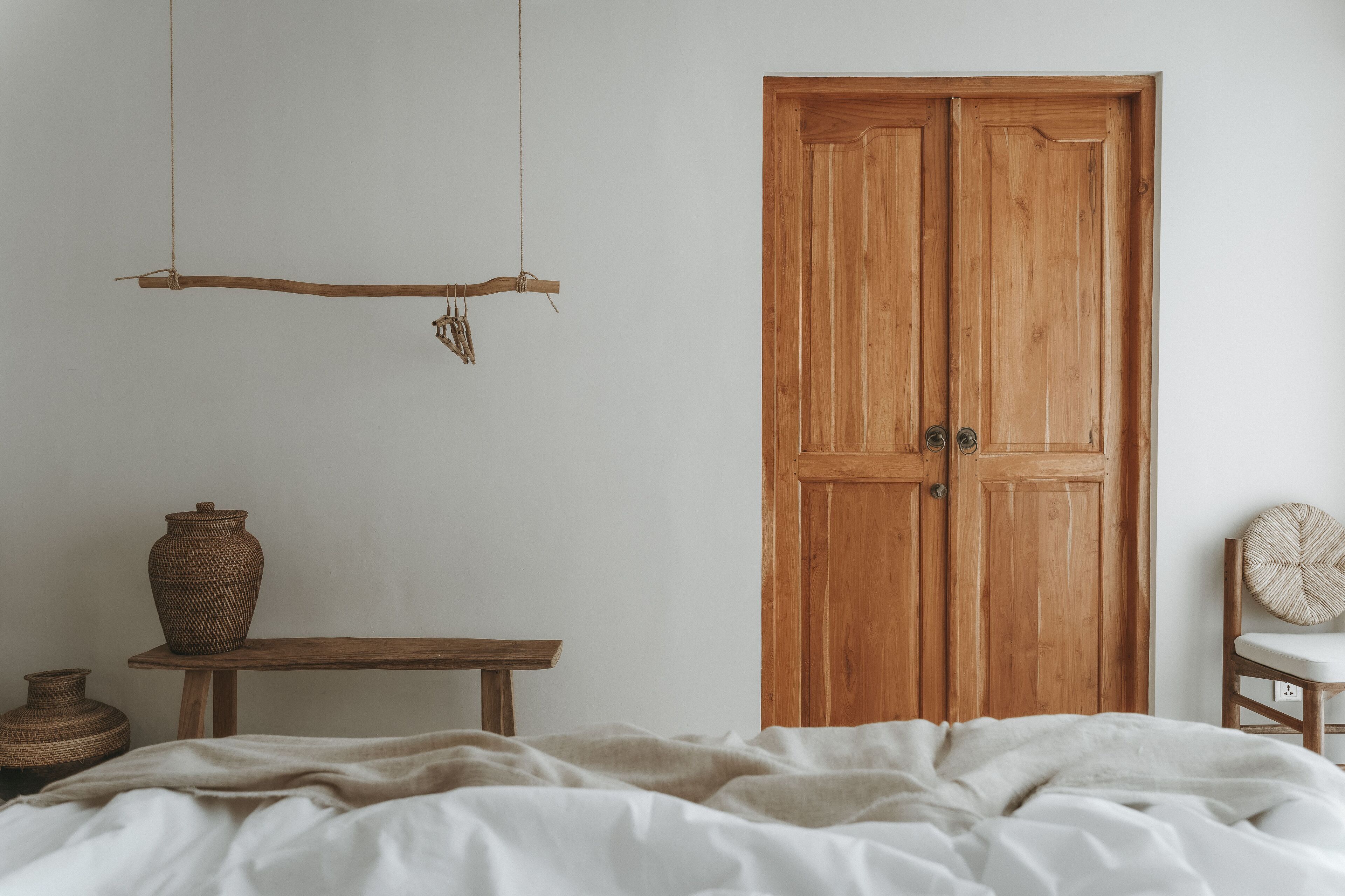 A bedroom with a wooden wardrobe, a hanging branch, a woven basket, and a wicker chair.