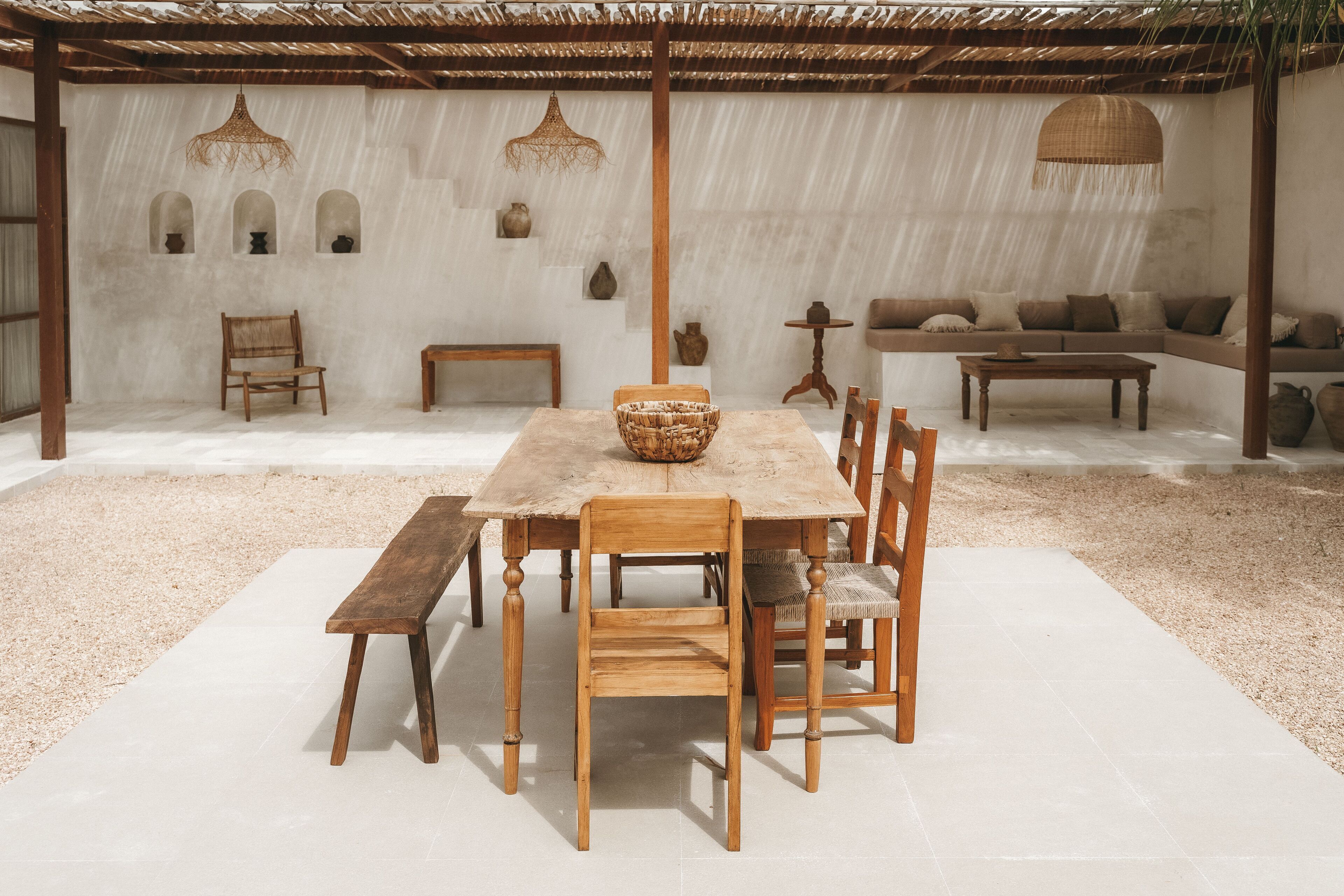 A rustic outdoor dining area with a wooden table and chairs, a woven basket, and a bench.