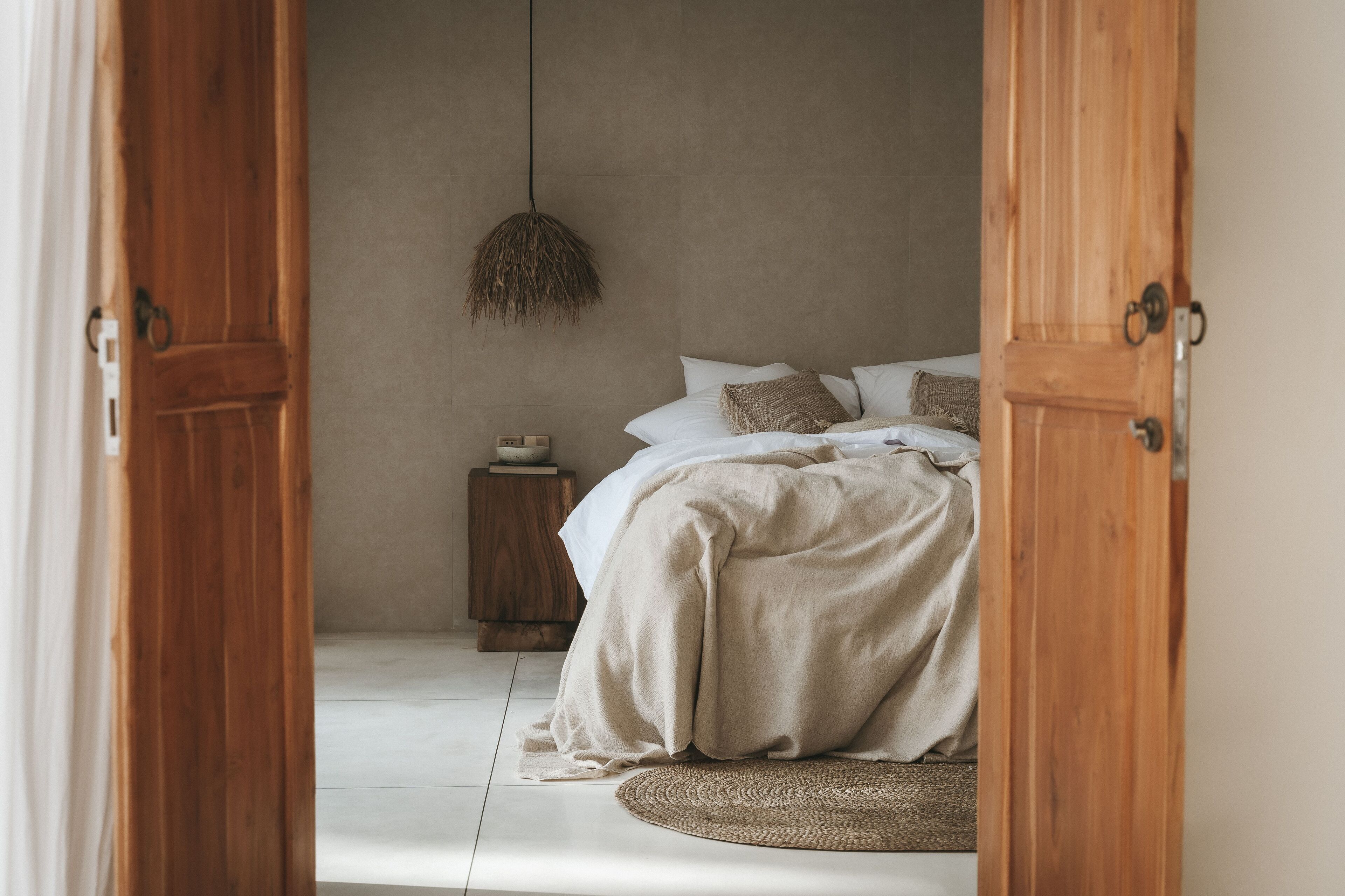 A bedroom with a bed, a hanging light fixture, a wooden nightstand, and a round rug.