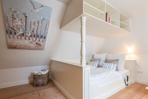 Un dormitorio con cama, mesita de noche, lámpara, un cuadro y una cesta de mimbre.