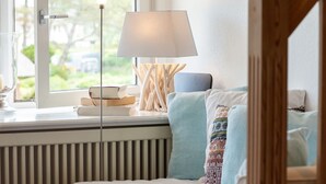 Ein gemütliches Zimmer mit einem Bett, einem Fenster mit Büchern und einer Lampe sowie Blick auf Grünflächen.