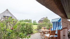 Eine Terrasse mit Tisch und Stühlen, einem Korbsessel und einem gestreiften Sonnensegel.