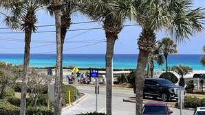 A coastal road with palm trees, a beach trail sign, and vehicles.