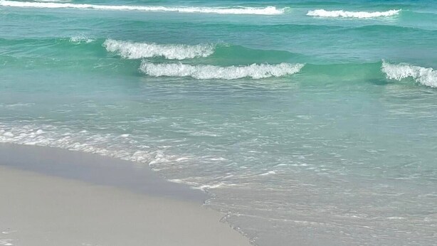 A beach with clear turquoise water and gentle waves.