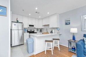 Une cuisine moderne avec des meubles blancs, un réfrigérateur en acier inoxydable, un four à micro-ondes et une cuisinière. On y trouve deux tabourets de bar et une poubelle.