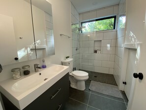 Une salle de bain moderne avec un lavabo blanc, des meubles sombres, des toilettes et un espace douche.