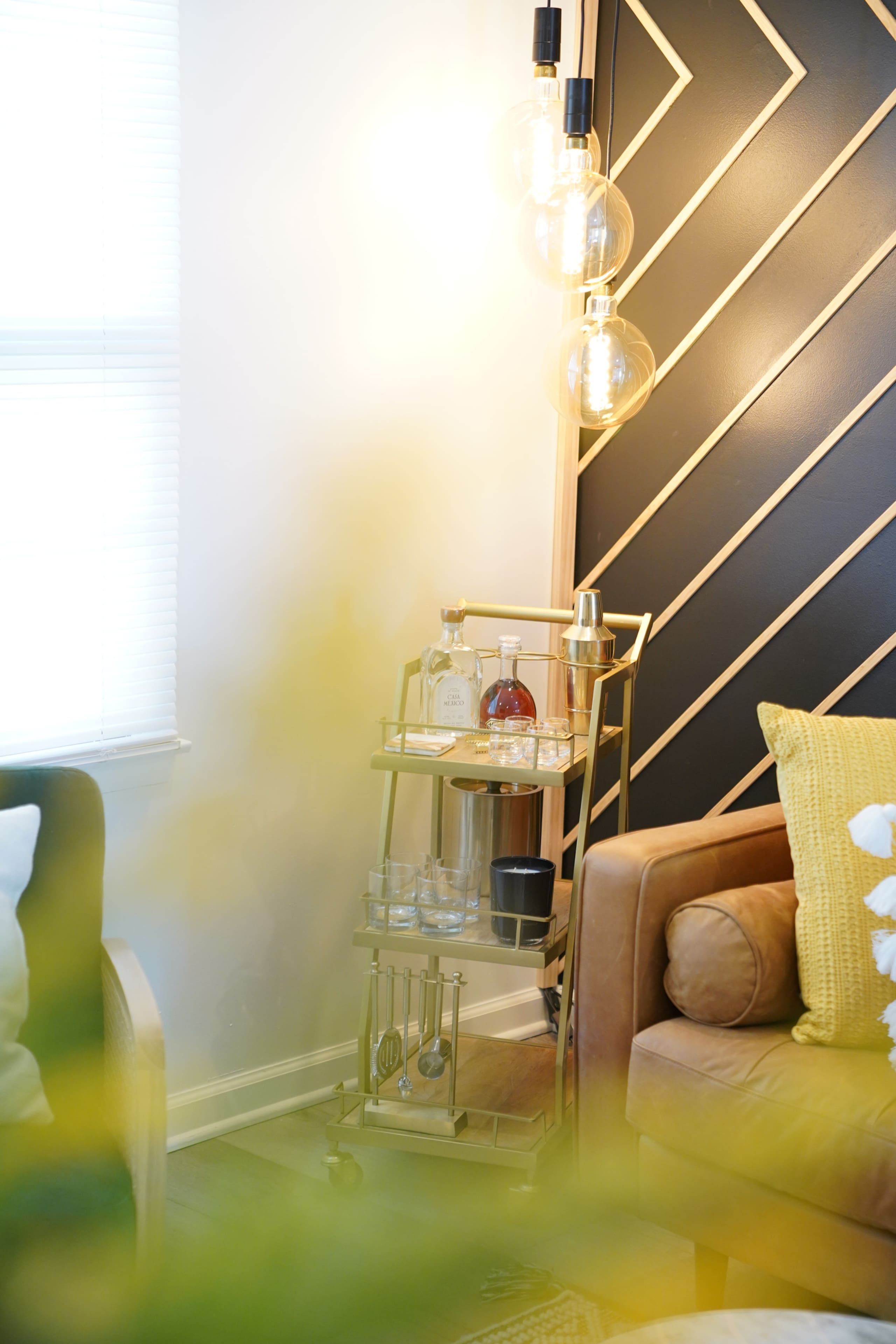 Ein modernes Wohnzimmer mit einer Wand im geometrischen Muster, einem Glastisch und einem Sofa mit einem gelben Kissen.