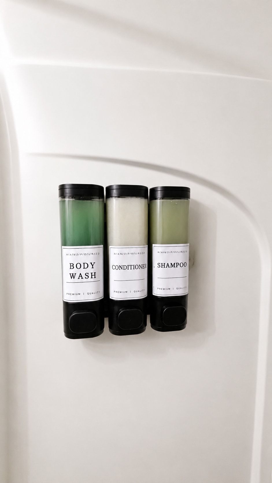 Drie flessen douchegel, conditioner en shampoo bevestigd aan een witte muur.