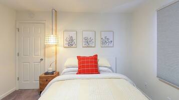Un dormitorio con cama, mesita de noche, lámpara, puerta y tres cuadros enmarcados.
