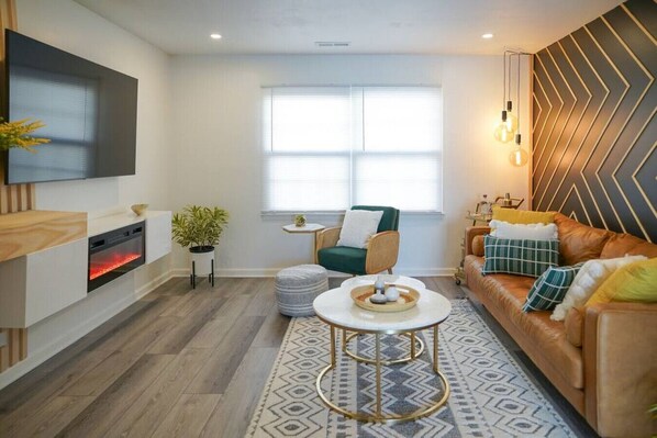 A modern living room with a fireplace, a sofa set, a television mounted on the wall, and a patterned rug.