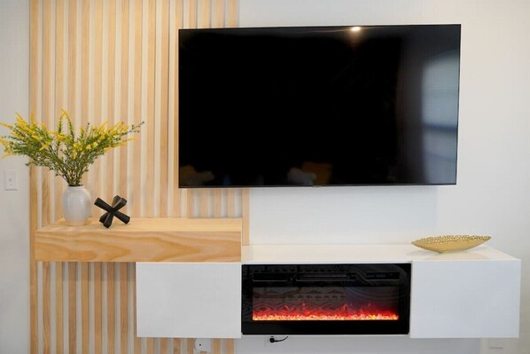 Una sala de estar moderna con un televisor de pantalla plana montado en la pared, una chimenea empotrada debajo y un estante de madera con un florero.
