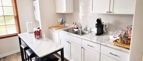 Una cocina moderna con armarios blancos, encimera de mármol, un lavabo y una cafetera.
