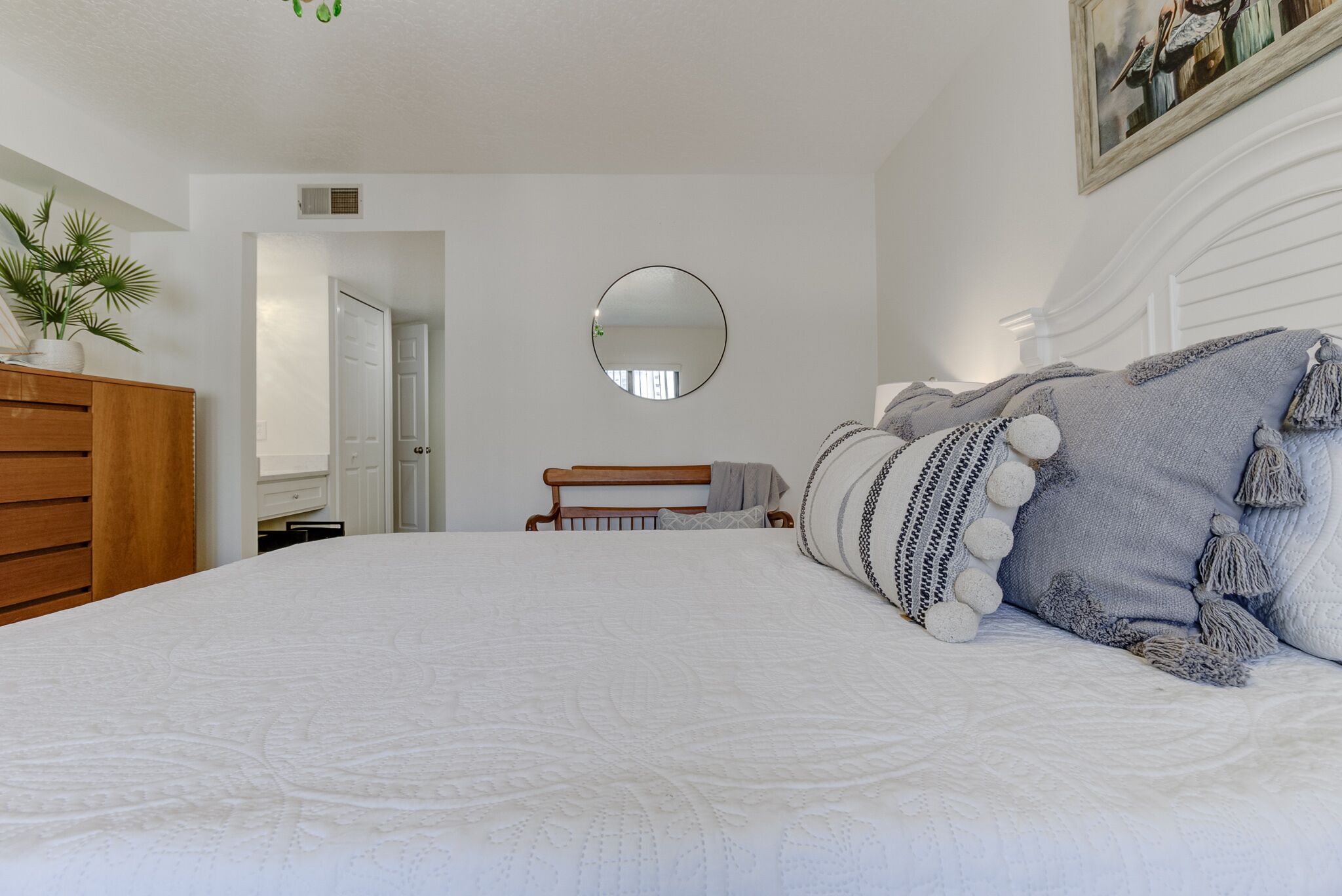A bedroom with a large bed, a wooden headboard, a round mirror, and a potted plant.