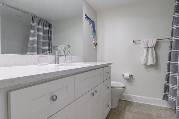 A bathroom with a white vanity, a mirror, a toilet, and a shower curtain.