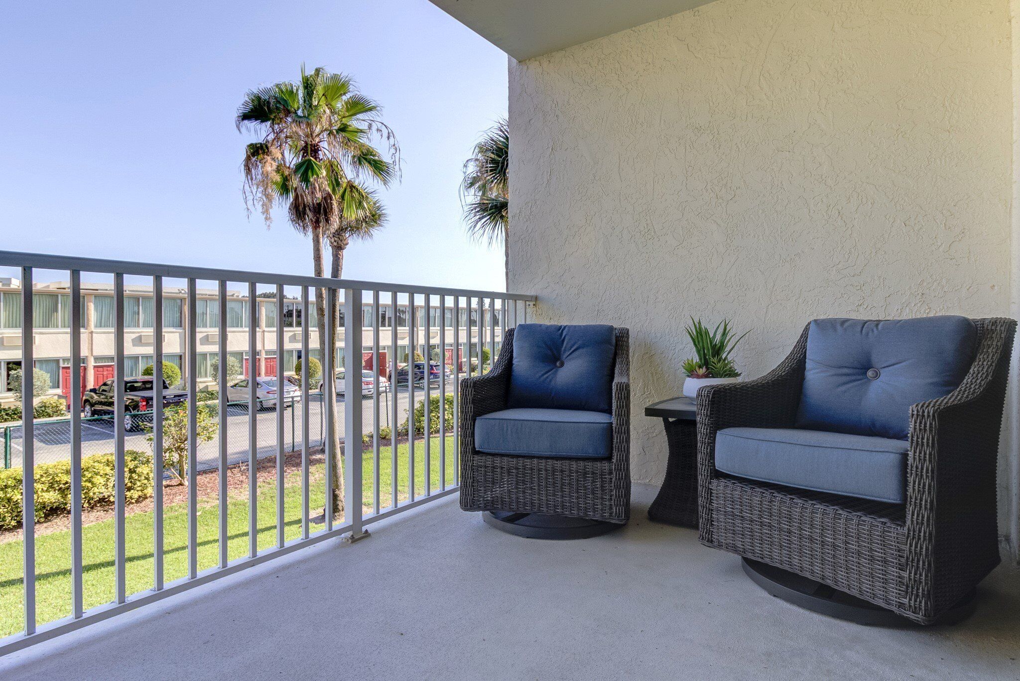 A balcony with two wicker chairs, a small table, and a potted plant.