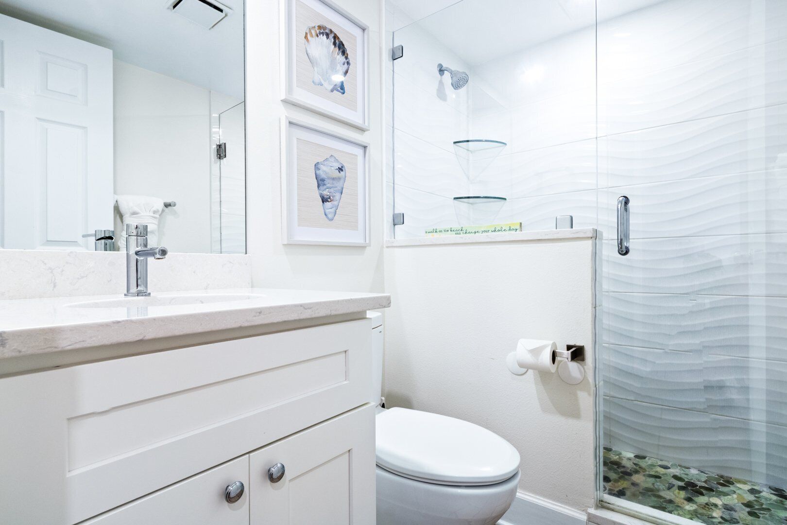 A bathroom with a white vanity, a toilet, a glass shower enclosure, and framed artwork on the wall.