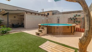 Een achtertuin met een houten jacuzzi, een overdekte patio en een zwembad.