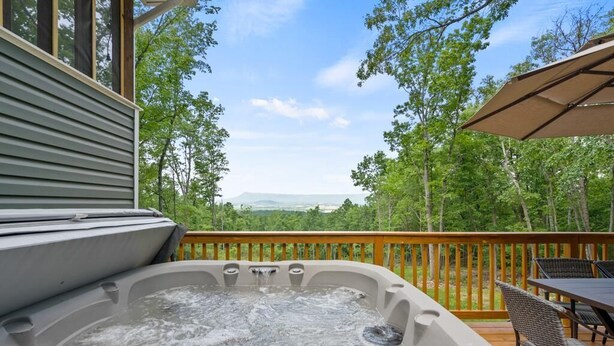 Un bain à remous sur une terrasse en bois, avec vue sur une forêt et des montagnes.