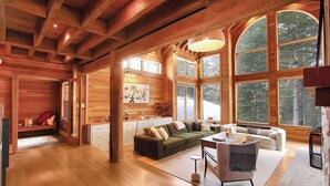 A spacious log cabin interior with a large living area, a fireplace, and large windows offering a view of the surrounding forest. - *TOP TIER* SUNDANCE LODGE - 7 Bed, 7 Bath, MOUNTAIN VIEWS (Sundance)