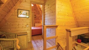 Une chambre confortable située dans les combles, avec des murs en bois, un lit, des meubles en osier et un tableau encadré accroché au mur.