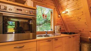 Une cuisine rustique aménagée dans une cabane en bois, avec un four en acier inoxydable, un évier et une fenêtre donnant sur un paysage verdoyant.
