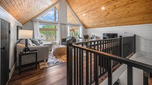 Uma ampla sala de estar em estilo loft, com pé direito alto, grandes janelas e piso de madeira.