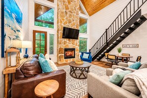 A spacious living room with a stone fireplace, leather sofas, a dining area, and a staircase.