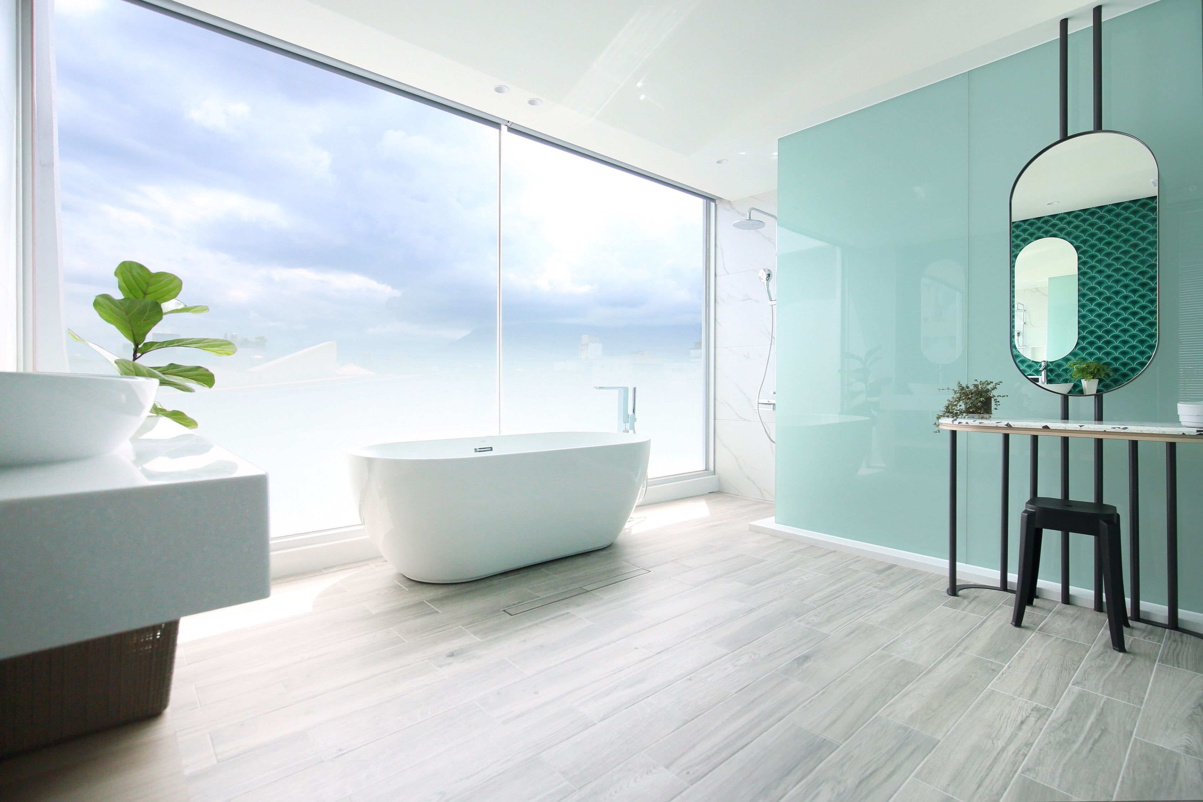 A modern bathroom with a freestanding bathtub, a large window, and a mirror with a geometric backsplash.