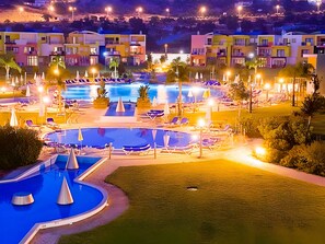 A resort with multiple swimming pools, sun loungers, and a well-lit landscape.
