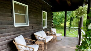 A wooden cabin with a porch featuring wicker chairs with white cushions.