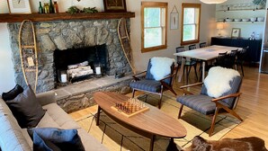 A cozy living room with a stone fireplace, a chessboard, and a dining area with a table and chairs.