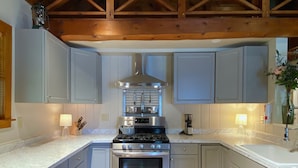 A kitchen with light blue cabinets, a stainless steel stove, and a wooden ceiling.