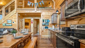 A wooden cabin interior with a dining area, kitchen, and loft bedroom. - Perfect Family Cabin for 4–5 • Kids' Loft, Arcade, Hot Tub, Easy Drive (Gatlinburg)