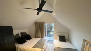 Un dormitorio con dos camas, ventilador de techo, puerta corrediza de vidrio a un balcón y un armario de color oscuro.