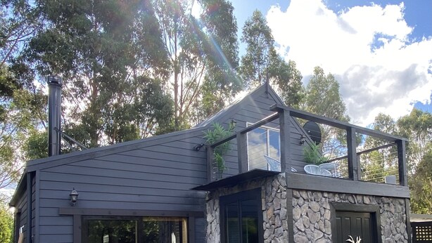 Una casa moderna con fachada de piedra, grandes puertas correderas de vidrio y un porche pequeño.