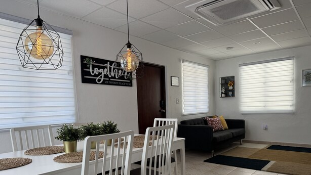 A modern dining area with a white table, chairs, and pendant lighting. - Modern 3BR Home in Fontana Village with Power & Water Backup (Carolina)
